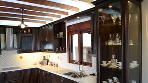 A modern kitchen with dark wood cabinets, a stainless steel sink, and a built-in glass display cabinet with white dishes. - Villa Bella Loukisia (Chalcis)