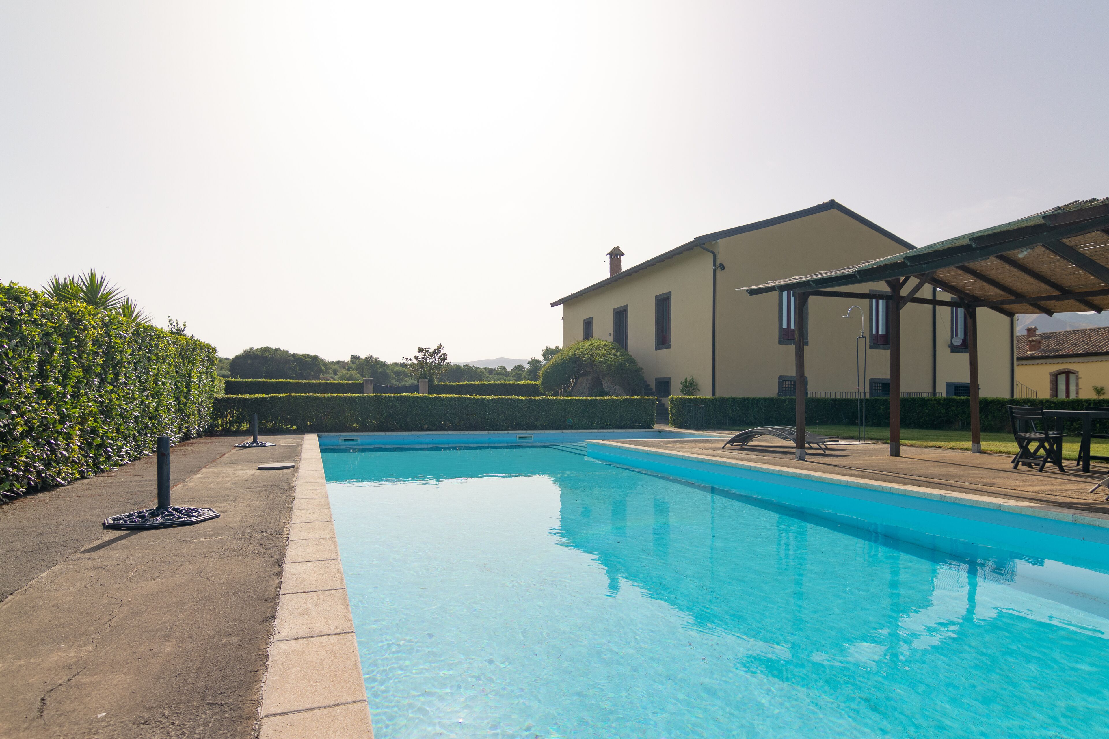 En swimmingpool med en klar blå vandoverflade, omgivet af en belagt område med en pergola.