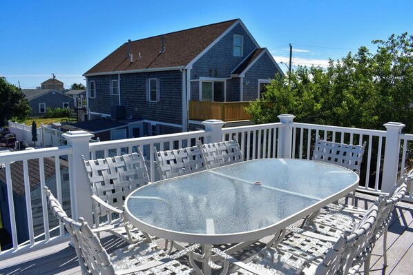 A deck with a glass-top table and white wicker chairs, surrounded by a white railing.