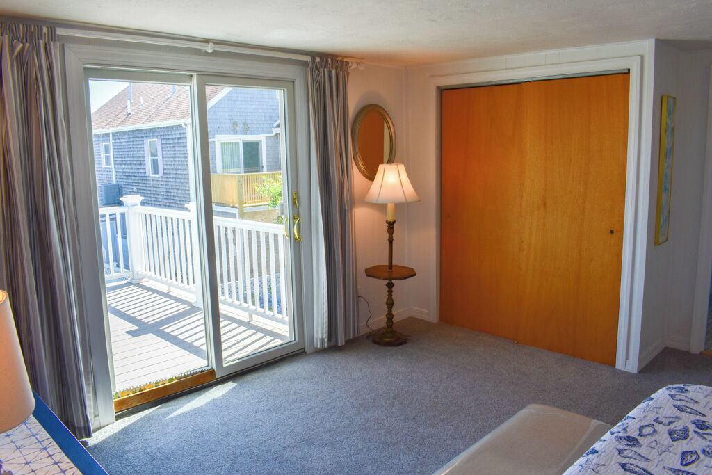 A bedroom with a sliding glass door to a balcony, a wooden door, a lamp, and a bed.