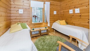 A cabin with two single beds, a small table, a lamp, and a view of a cabin through a window.