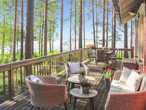A wooden deck with wicker furniture, a table, and chairs overlooking a body of water.