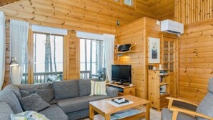 L’intérieur d’un chalet en bois chaleureux et accueillant, avec un canapé, une table basse, un téléviseur et une bibliothèque.