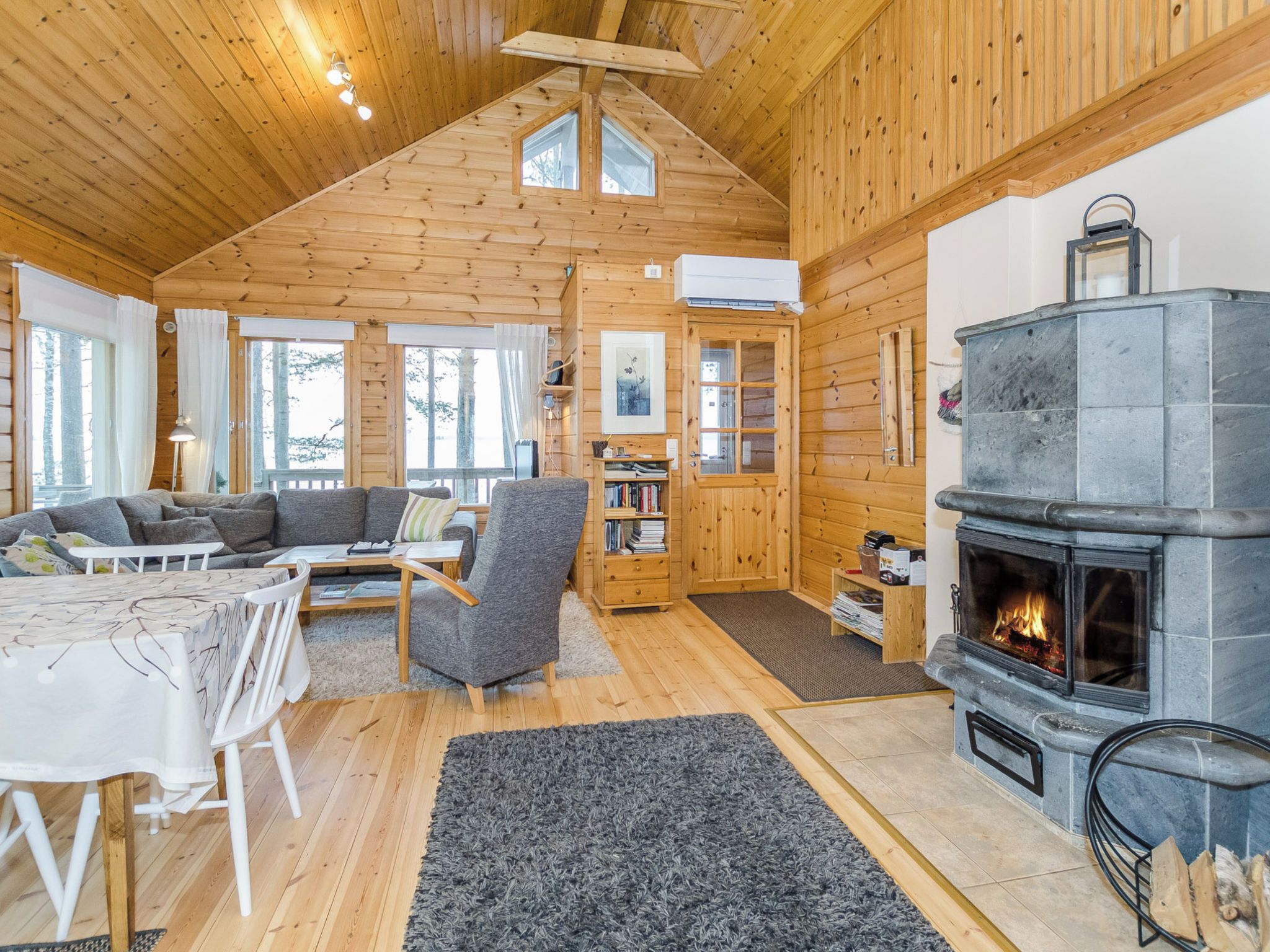 A cozy cabin interior with a wooden interior, a fireplace, a sofa, a dining table, and a bookshelf.