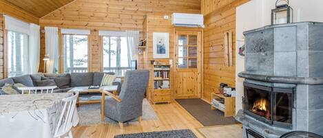 A cozy cabin interior with a wooden interior, a fireplace, a sofa, a dining table, and a bookshelf.