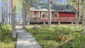 A cabin with a wooden deck and a covered porch, surrounded by a forest.