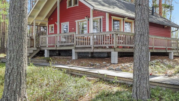 A red cabin with a porch, surrounded by trees.