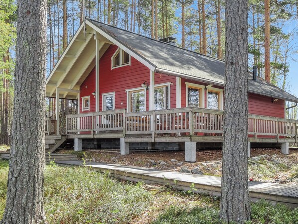 A red cabin with a porch, surrounded by trees.
