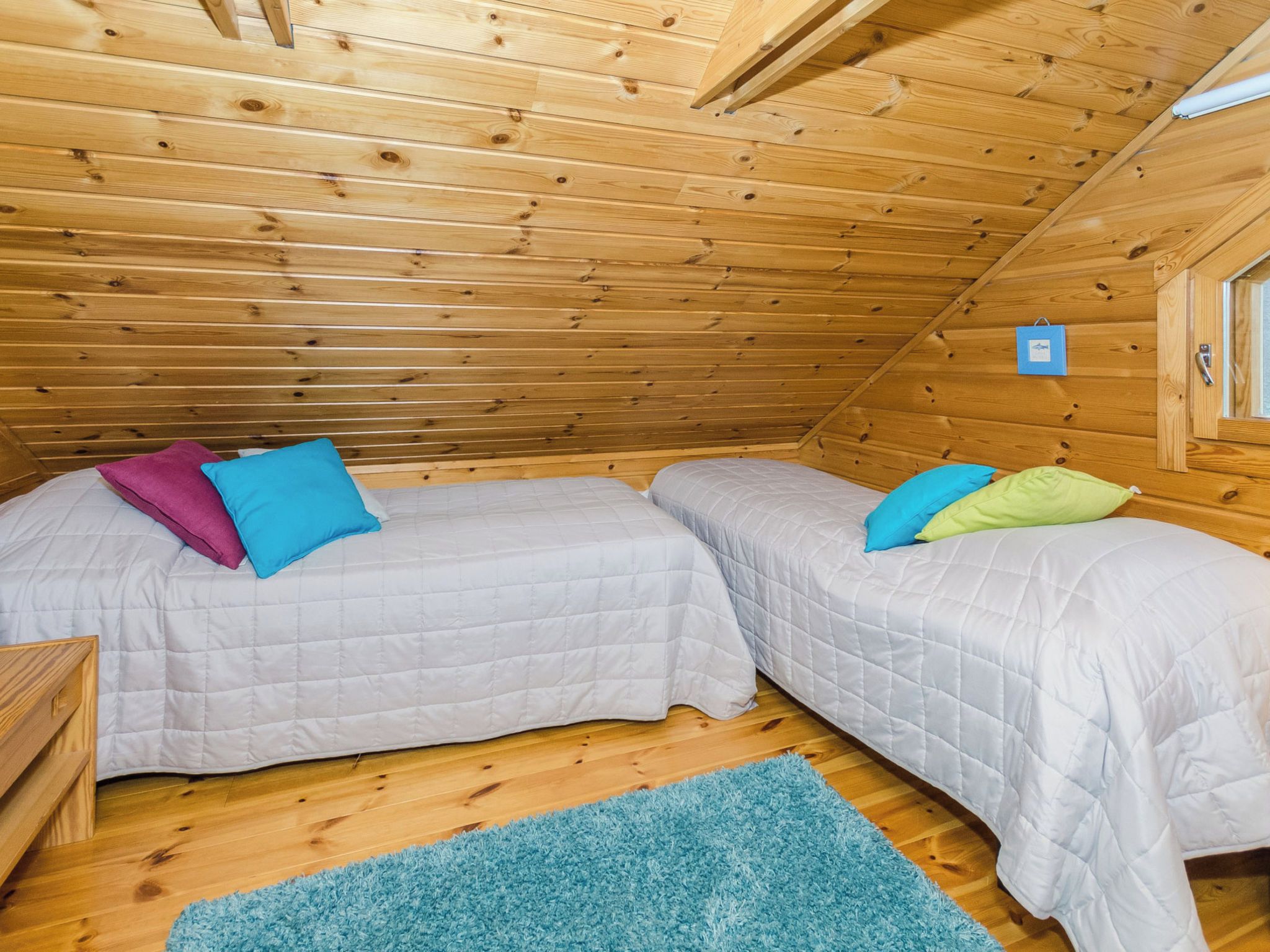 A small, cozy room with two beds, a blue rug, and wooden walls.