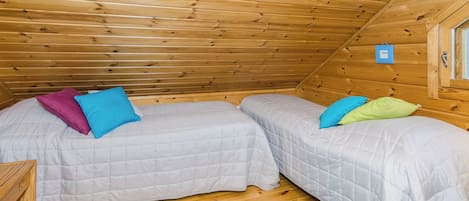 A small, cozy room with two beds, a blue rug, and wooden walls.