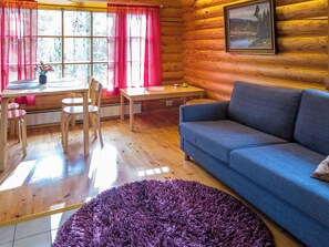 Interior acogedor de una cabaña con comedor, sofá y un amplio ventanal con cortinas.