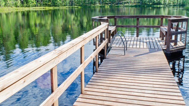 A wooden dock extending into a calm lake surrounded by dense green trees.