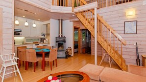 A cozy cabin interior with a dining area, a fireplace, a staircase, and a living room with a sofa and a coffee table.