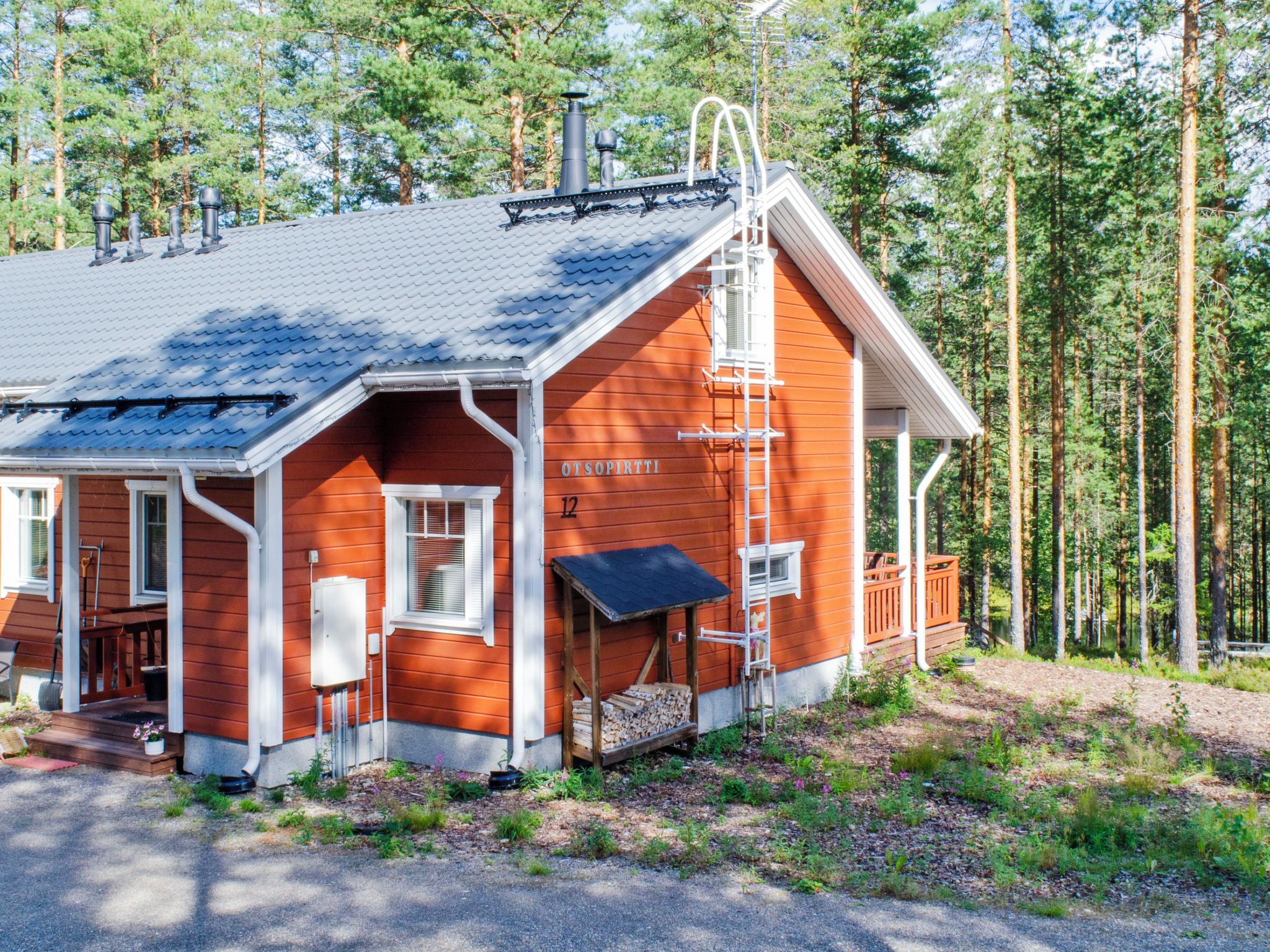 Une cabane en bois avec une cheminée, une véranda et une échelle menant au toit.