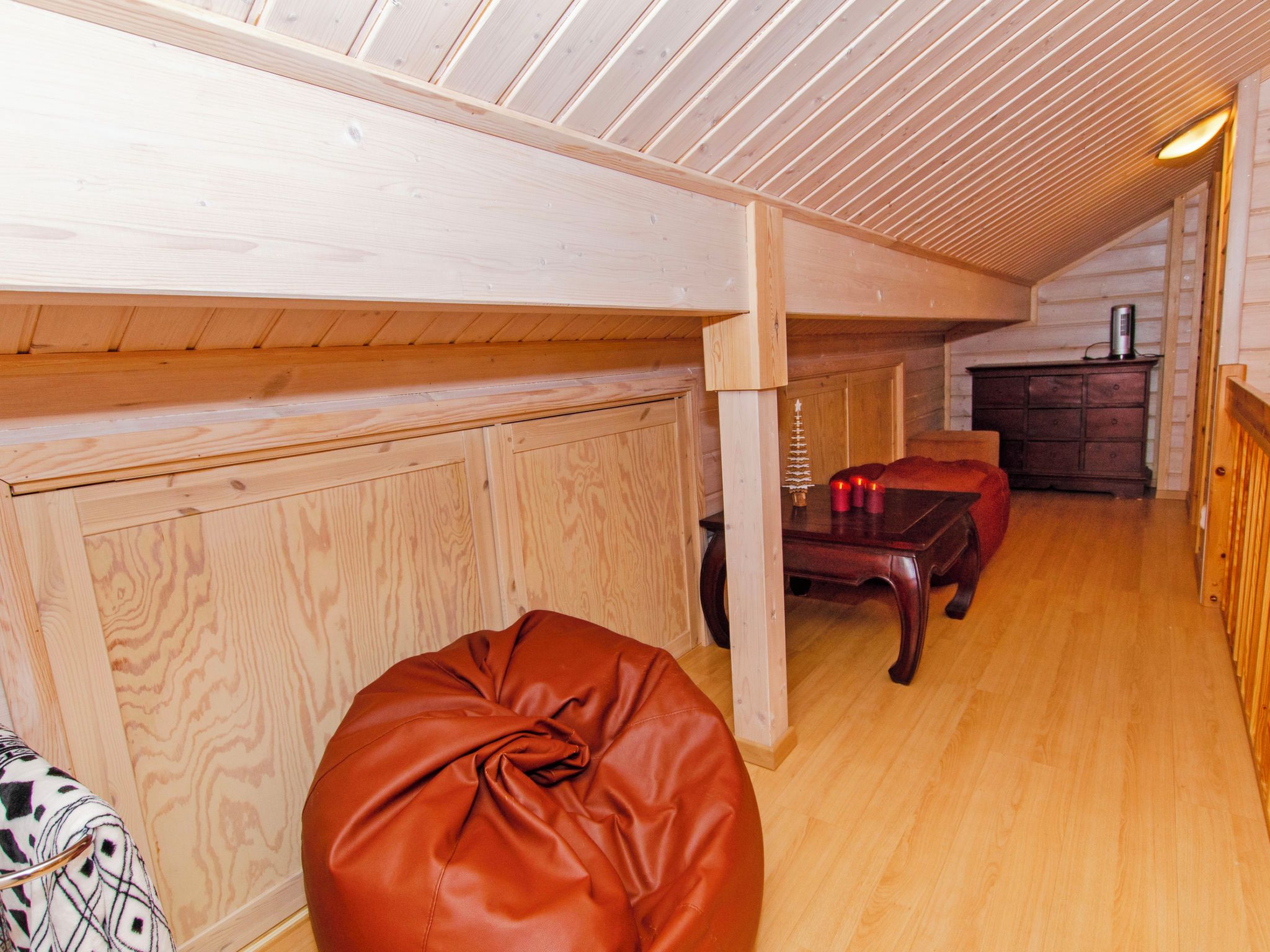 Ein Holzinnenraum mit hoher Decke, einem Lederhocker, einem Holzkasten und einem Kamin.