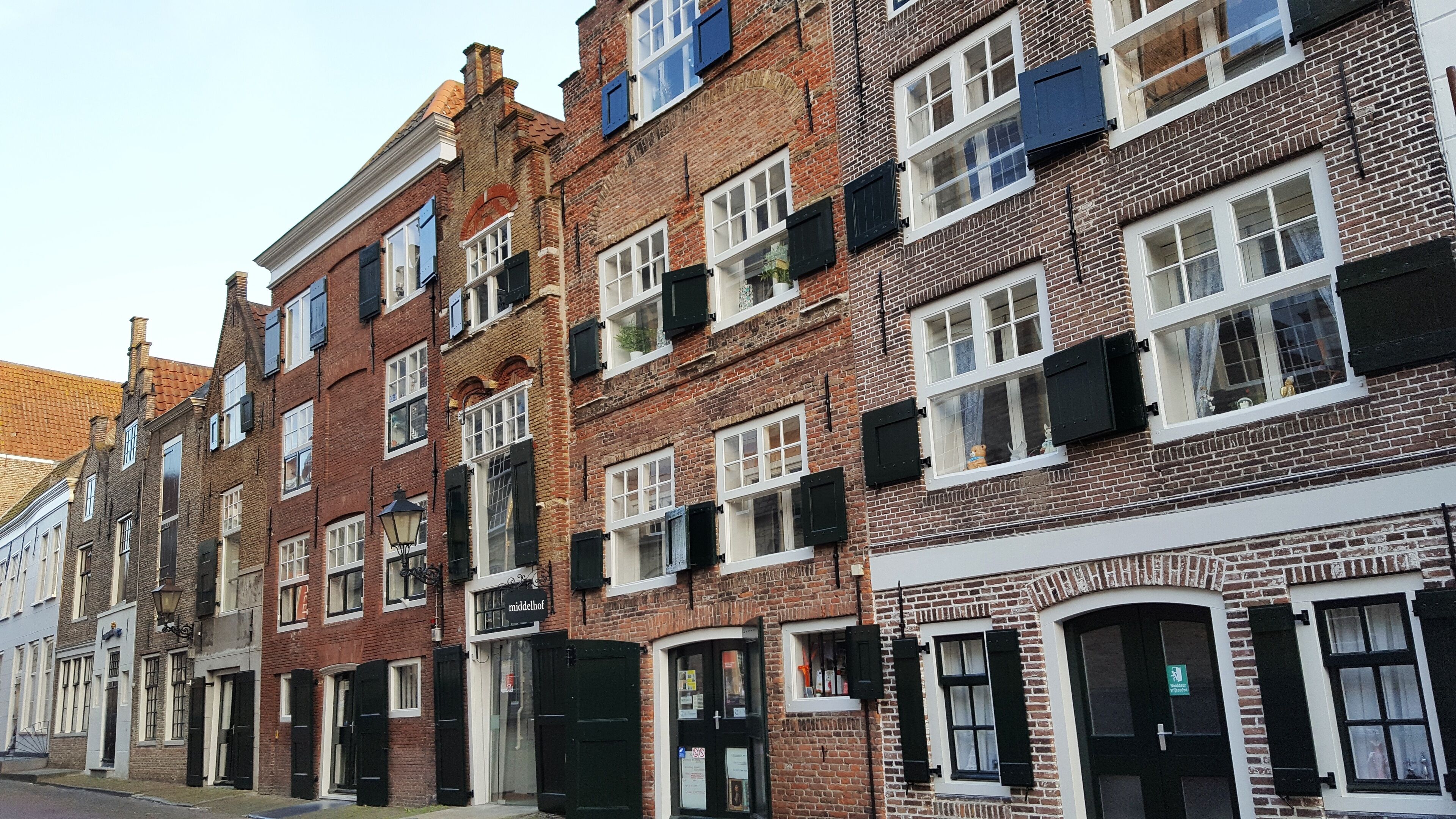 Une rangée de bâtiments traditionnels en briques, à plusieurs étages, avec des encadrements de fenêtres blancs et des volets noirs.