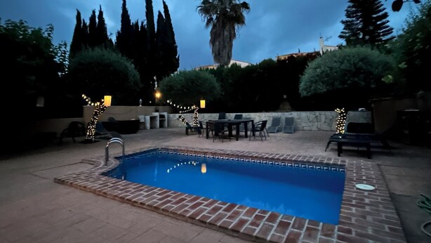 A rectangular swimming pool with a tiled edge, surrounded by a brick patio. There are outdoor seating areas with tables and chairs, and string lights along the patio's edge. - Fabulous family friendly 4 bed villa with private pool (Alcaucín)