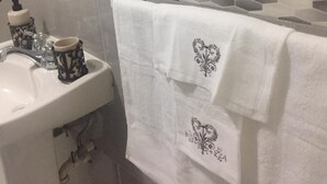 Un baño con lavamanos blanco, espejo y toallero con toallas blancas.
