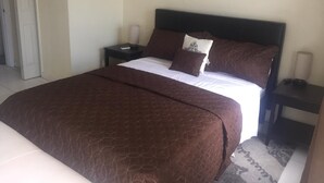 Una cama bien hecha con un edredón marrón, dos mesitas de noche con lámparas y una puerta al fondo.