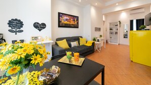 Uma sala de estar moderna com um sofá, uma mesa de centro e um armário amarelo. Há objetos decorativos nas paredes e um quadro acima do sofá.