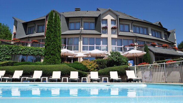 Un hôtel doté d’une piscine, de nombreux balcons ornés de jardinières et de parasols.