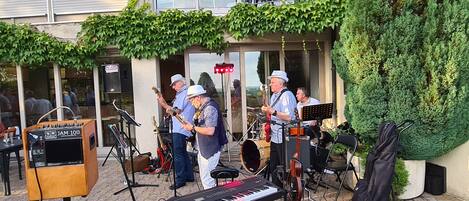 An outdoor music performance with a keyboard, guitar, and drums set up on a paved area.