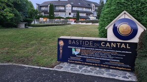 Une enseigne indiquant « Bastide du Cantal », avec un immeuble d’habitation visible en arrière-plan.