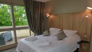 Une chambre d’hôtel avec un grand lit, une fenêtre avec des rideaux, une tête de lit en bois et une table de chevet avec une lampe.