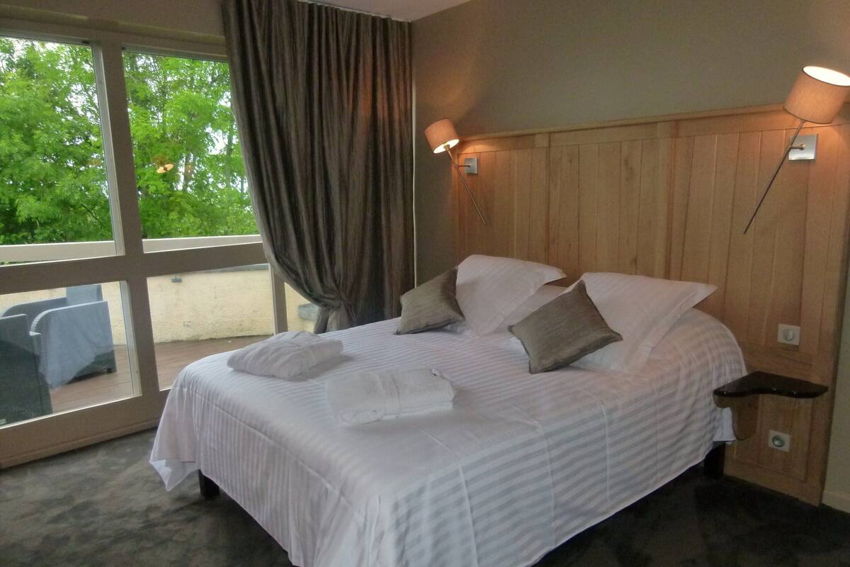 Ein Hotelzimmer mit einem großen Bett, einem Fenster mit Vorhängen, einem Holzkopfseitenverkleidung und einem Nachttisch mit Lampe.