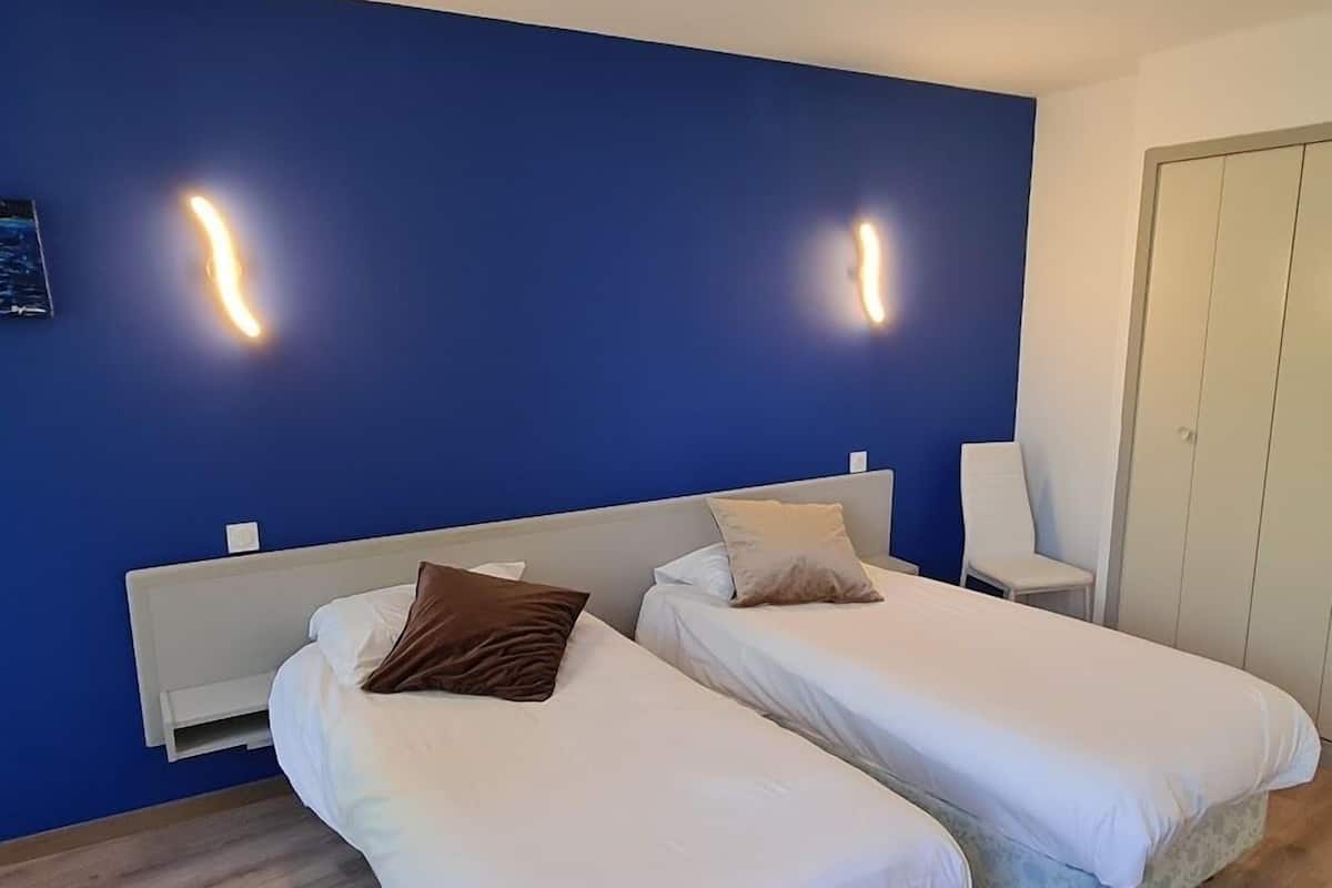 Ein Hotelzimmer mit zwei Einzelbetten, einem weißen Schrank und einem Sessel.