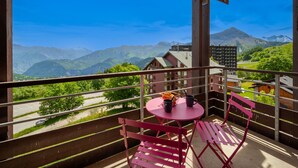 Un balcón con mesa y sillas, con vistas a un paisaje montañoso.