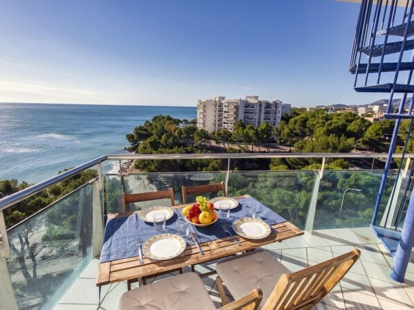 A dining table set on a balcony with a view of the sea and buildings in the background.