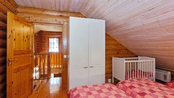 A bedroom with a wooden ceiling, a white wardrobe, a crib, and a checkered bedspread.