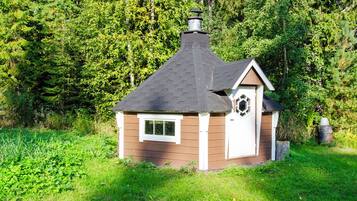 Eine kleine Holzhütte mit Satteldach und Schornstein, umgeben von dichtem Wald.
