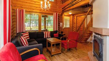 Ein Blockhaus-Interieur mit Kamin, Holzdielen, einer Sofagarnitur und einer Treppe.