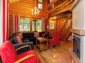 A log cabin interior with a fireplace, wooden floors, a sofa set, and a staircase.