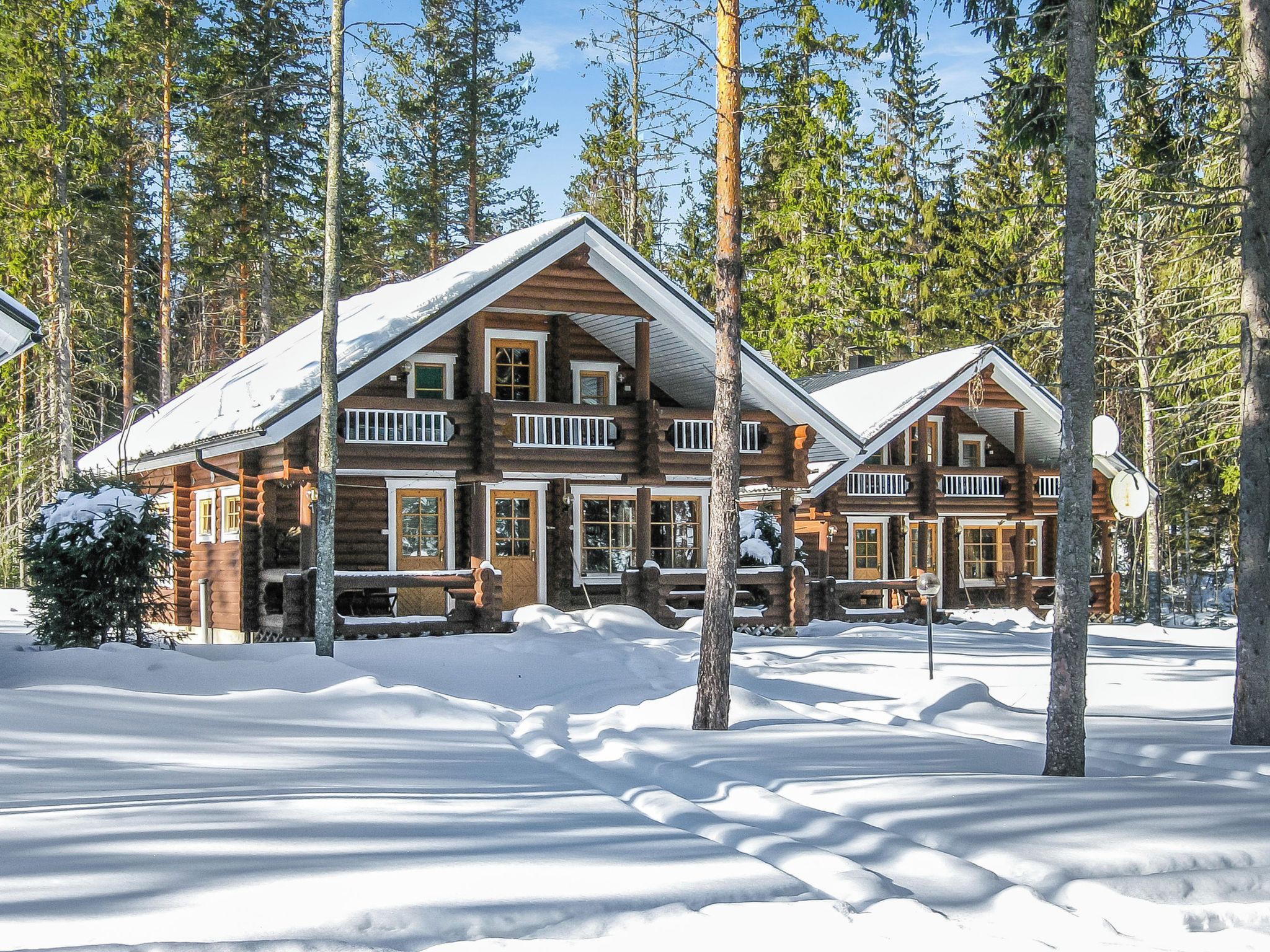 A log cabin with a balcony, surrounded by snow and trees.