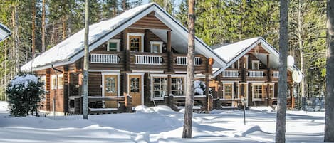 A log cabin with a balcony, surrounded by snow and trees.