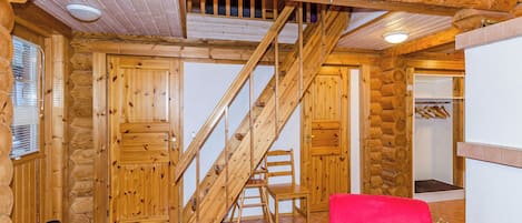 Interior de cabana de tronco com escada de madeira, uma cadeira vermelha e mesa de madeira com revistas.