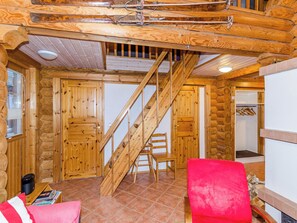 A log cabin interior with a wooden staircase, a red chair, and a wooden table with magazines.