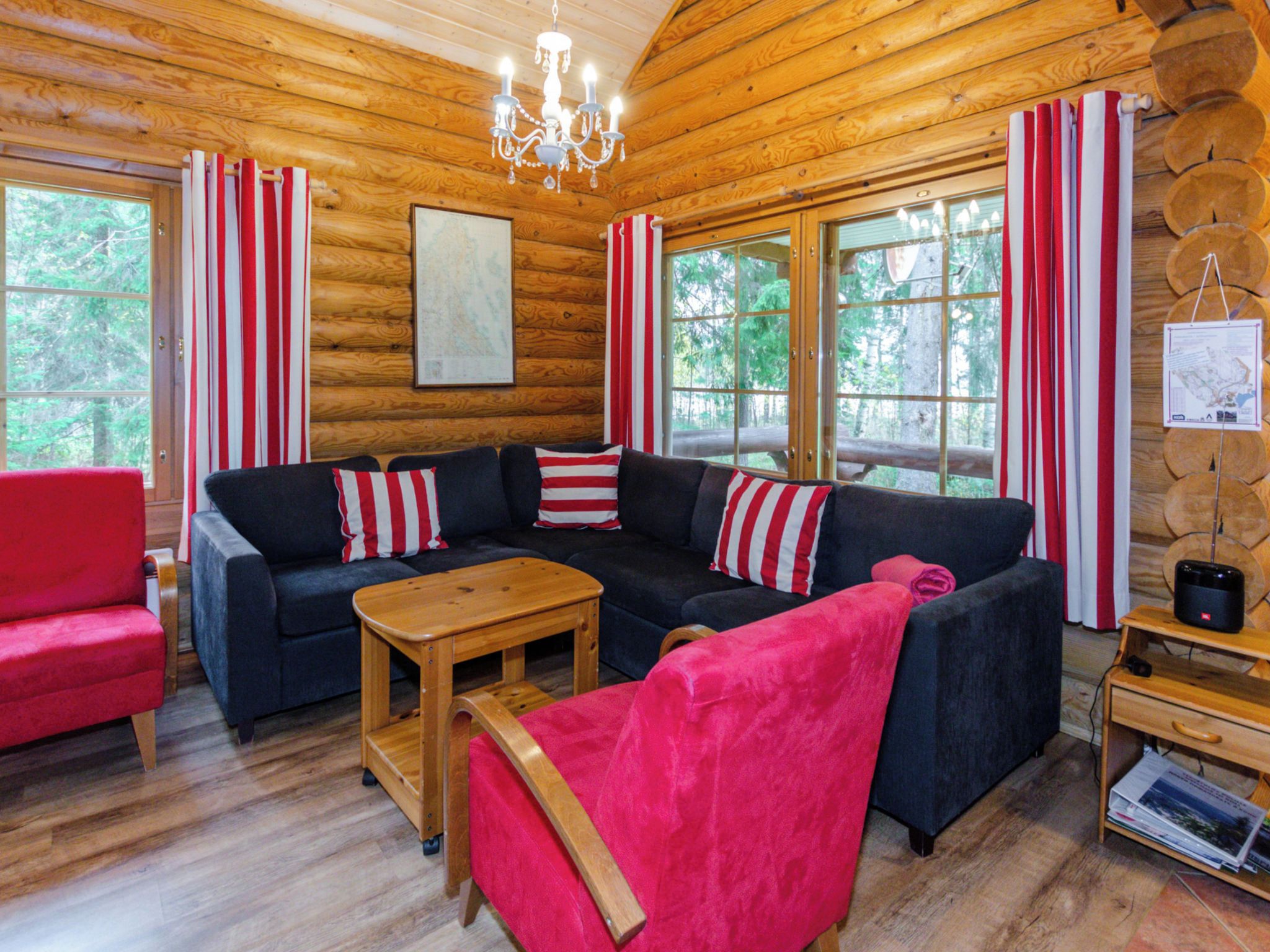 Ein Holzblockhaus-Interieur mit einer Eckcouch, einem roten Sessel, einem Holztisch und einer Kristallleuchtre.