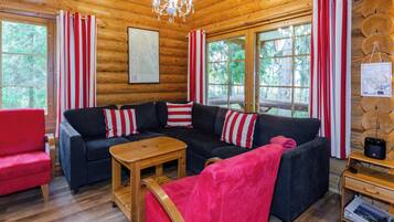 Ein Holzblockhaus-Interieur mit einer Eckcouch, einem roten Sessel, einem Holztisch und einer Kristallleuchtre.
