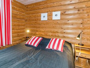 Een houten kamer met een bed, twee bedlampjes en een rood-wit gestreept gordijn.