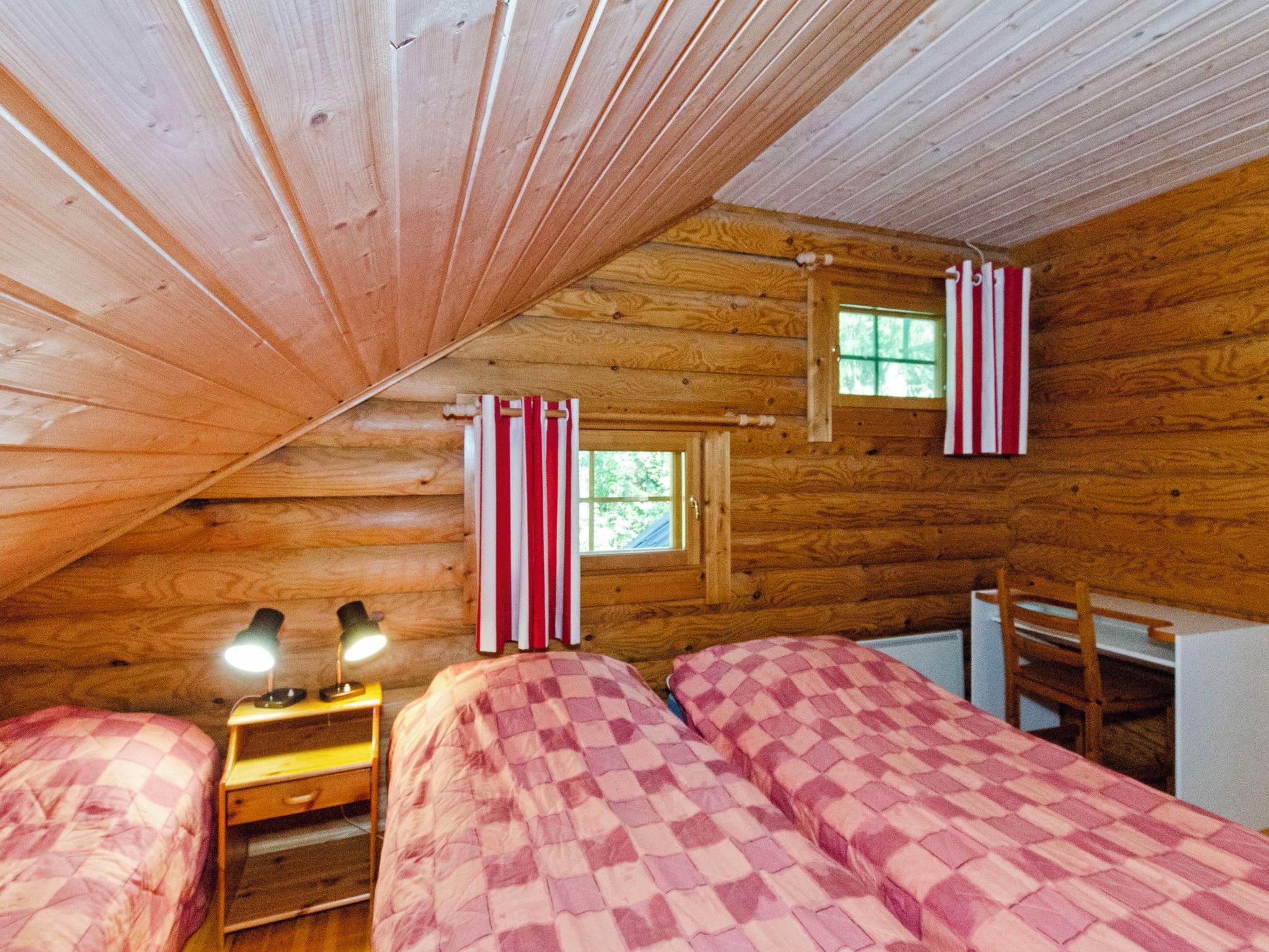 A cozy cabin bedroom with two beds, a desk, and a window with curtains.