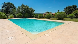 Una piscina rettangolare con bordo piastrellato, immersa nel verde sotto un cielo azzurro intenso.
