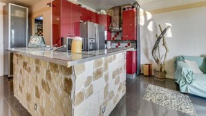 Una cucina moderna con mobili rossi, un'isola in pietra e vista sull'area soggiorno.