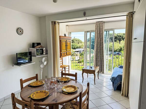 A dining area with a round table set for four, a microwave, a fan, and a cabinet.