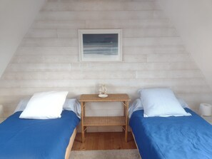 A bedroom with two beds, a small table with a lamp, a picture on the wall, and a wooden floor.