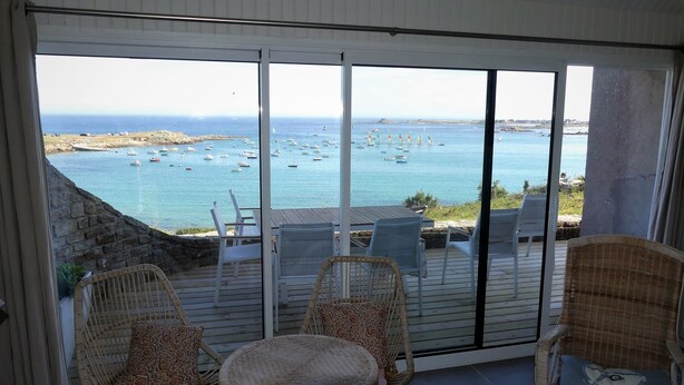 A balcony with wicker chairs and a table, overlooking a coastal area with boats and a rocky shoreline. - Character house with 180° panoramic sea view - Côte Sauvage de Portsall (Landunvez)