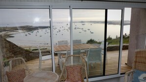 A balcony with wicker furniture, a wooden table, and a view of boats on the water. - Character house with 180° panoramic sea view - Côte Sauvage de Portsall (Landunvez)